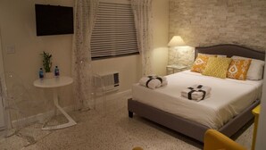 A hotel room with a bed, a TV mounted on the wall, a small table with a lamp, and a chair. - Beach Getaway, Cozy Studio Villa #2 (Lauderdale-by-the-Sea)