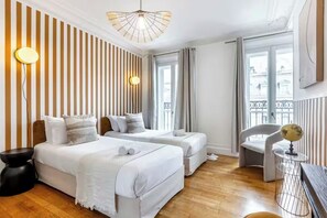 A hotel room with two beds, a round table with a globe, a chair, a large window with curtains, and a striped wall.