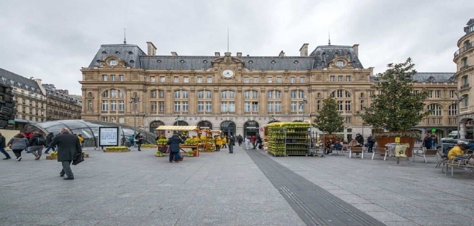 A historic building with a central clock tower, surrounded by a public square with vendors and seating areas.