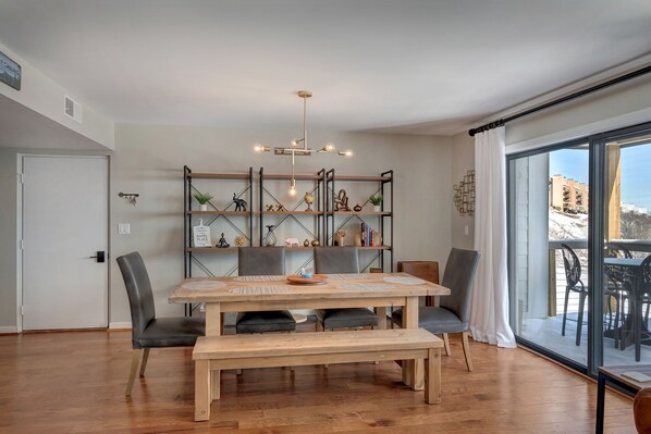 A dining area with a wooden table, grey upholstered chairs, a bench, and a modern chandelier.