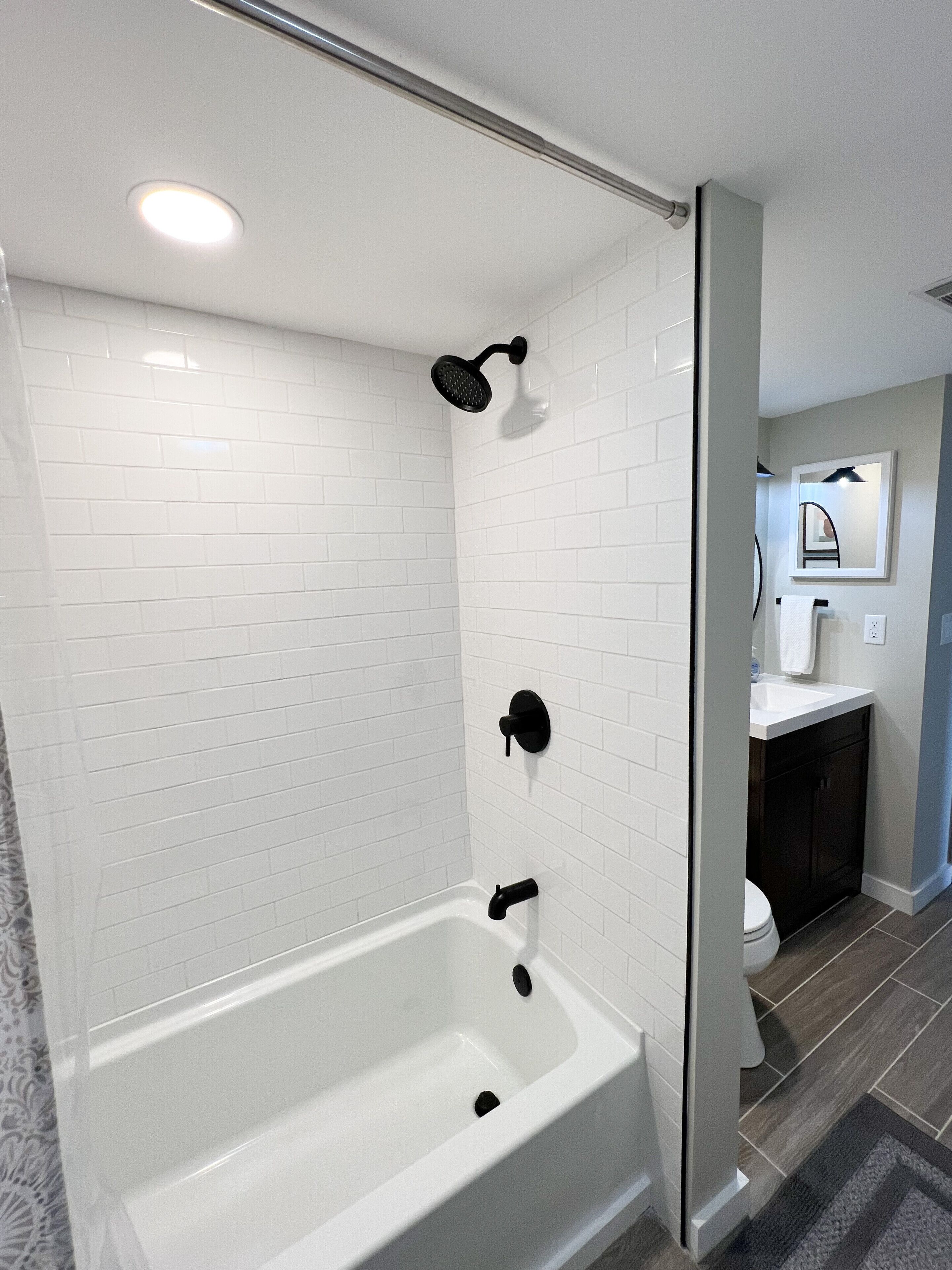A modern bathroom with a white bathtub, black fixtures, and a tiled shower area.