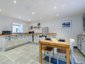 A modern kitchen with white cabinets, a wooden countertop, a built-in oven, and a dining area with a table and chairs.