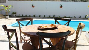 A round wooden table with chairs around a swimming pool. - Casa Barramares em Cotovelo com piscina (Parnamirim)