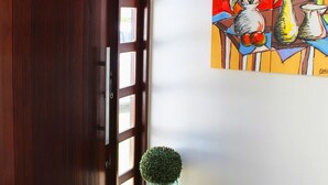 A wooden door with a glass panel, a small potted plant, and a colorful abstract painting on the wall. - Casa Barramares em Cotovelo com piscina (Parnamirim)