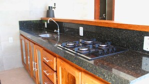 A kitchen with a granite countertop, a stainless steel sink, and a gas stove. - Casa Barramares em Cotovelo com piscina (Parnamirim)