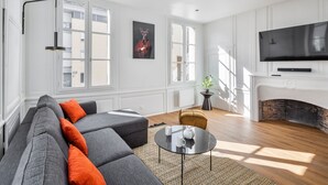 Ein modernes Wohnzimmer mit einem Ecksofa, einem runden Couchtisch, einem Kamin und einem großen Fernseher.