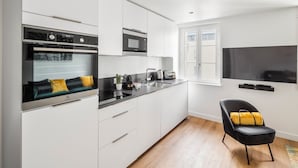 A modern kitchen with white cabinetry, a built-in oven, a microwave, and a large flat-screen TV mounted on the wall. - Neruda - Le 31 bis - Appt proche centre Rennes (Rennes)