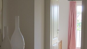 Un couloir avec une armoire en bois, une porte donnant sur une pièce avec un rideau à rayures, et une vue sur un balcon.