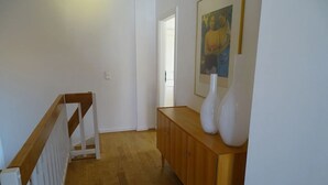Un couloir avec un escalier en bois, une porte blanche et un meuble en bois orné de vases.