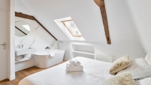Un dormitorio con tragaluz, un espejo redondo, una bañera blanca y una cama bien hecha.