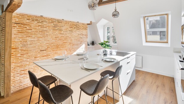 Una cocina moderna con pared de ladrillo decorativa, armarios blancos y una isla grande con taburetes de bar.