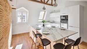 Una cocina moderna con una isla de mármol, vigas de madera y un ventanal grande.
