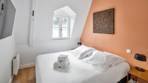 Une chambre à coucher comprenant un lit, une fenêtre, une œuvre d’art accrochée au mur, une table de chevet avec une lampe et un radiateur.