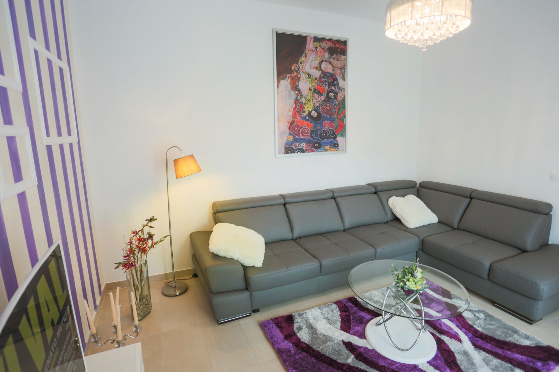 A modern living room with a grey sectional sofa, a glass coffee table, and a colorful abstract painting on the wall.