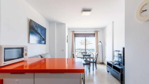 A modern kitchen with a microwave, a dining table with chairs, a TV, and a large window with curtains. - A&n   Seaport     1a (Caleta de velez)