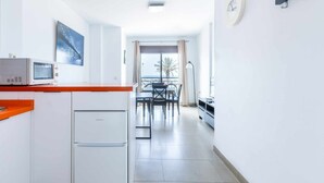 A modern kitchen with white cabinets, a microwave, and a small refrigerator. There is a dining area with a table and chairs, and a view of the outside through a window. - A&n   Seaport     1a (Caleta de velez)
