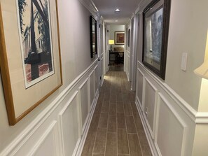 A hallway with framed pictures on the walls, a tiled floor, and a door at the end leading to another room.