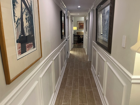 A hallway with framed pictures on the walls, a tiled floor, and a door at the end leading to another room.