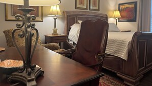 Ein Hotelzimmer mit einem hölzernen Bett, zwei Nachttischen mit Lampen, einem Sessel und einem Schreibtisch mit Lampe.