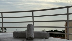 A bed with a rolled towel and pillows, a railing, and a view of the sea and buildings. - A&n    Seaport    1b  (Caleta de velez)