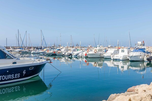 A marina with multiple boats docked, calm water, and a clear sky.
