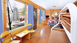 A cabin with a wooden interior, a bed with a patterned blanket, a television, and a dining area with a table and chairs. - Gorgeous Views, RMNP, Close to Downtown Estes Park, Real Log Cabin- Longs Peak Cabin (Estes Park)