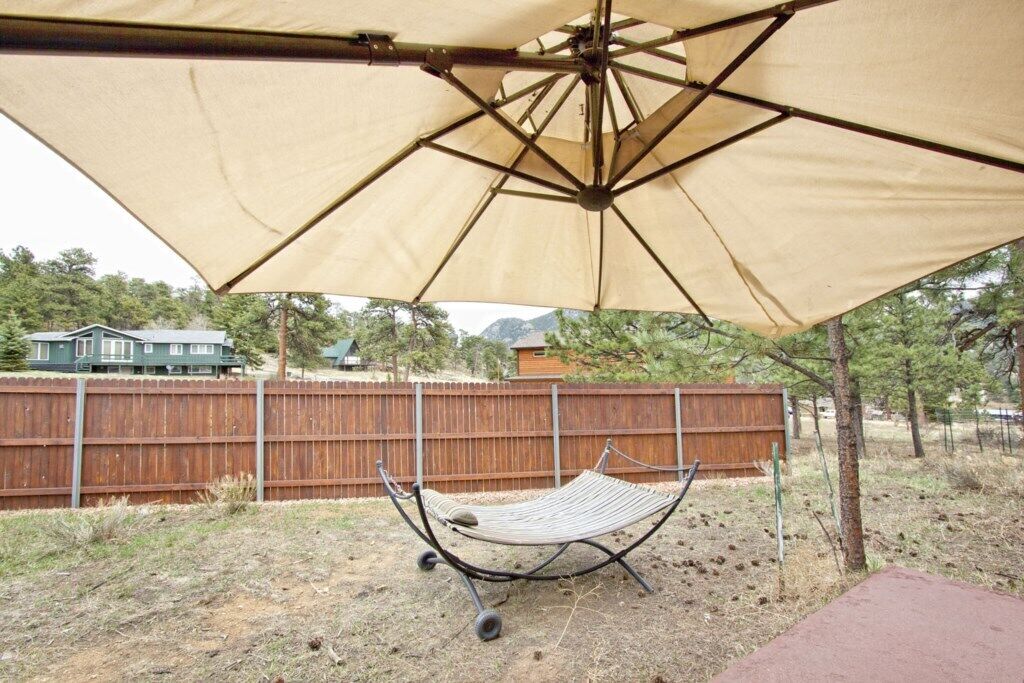 A hammock under a large canopy in a backyard with a wooden fence and trees in the background.