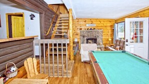 A cozy room with a wooden staircase, a fireplace, a pool table, and a door leading outside. - Gorgeous Views, RMNP, Close to Downtown Estes Park, Real Log Cabin- Longs Peak Cabin (Estes Park)