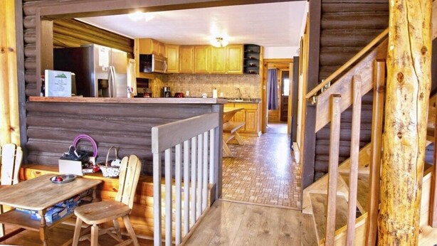 A log cabin interior with a kitchen area, wooden dining table, and chairs. - Gorgeous Views, RMNP, Close to Downtown Estes Park, Real Log Cabin- Longs Peak Cabin (Estes Park)