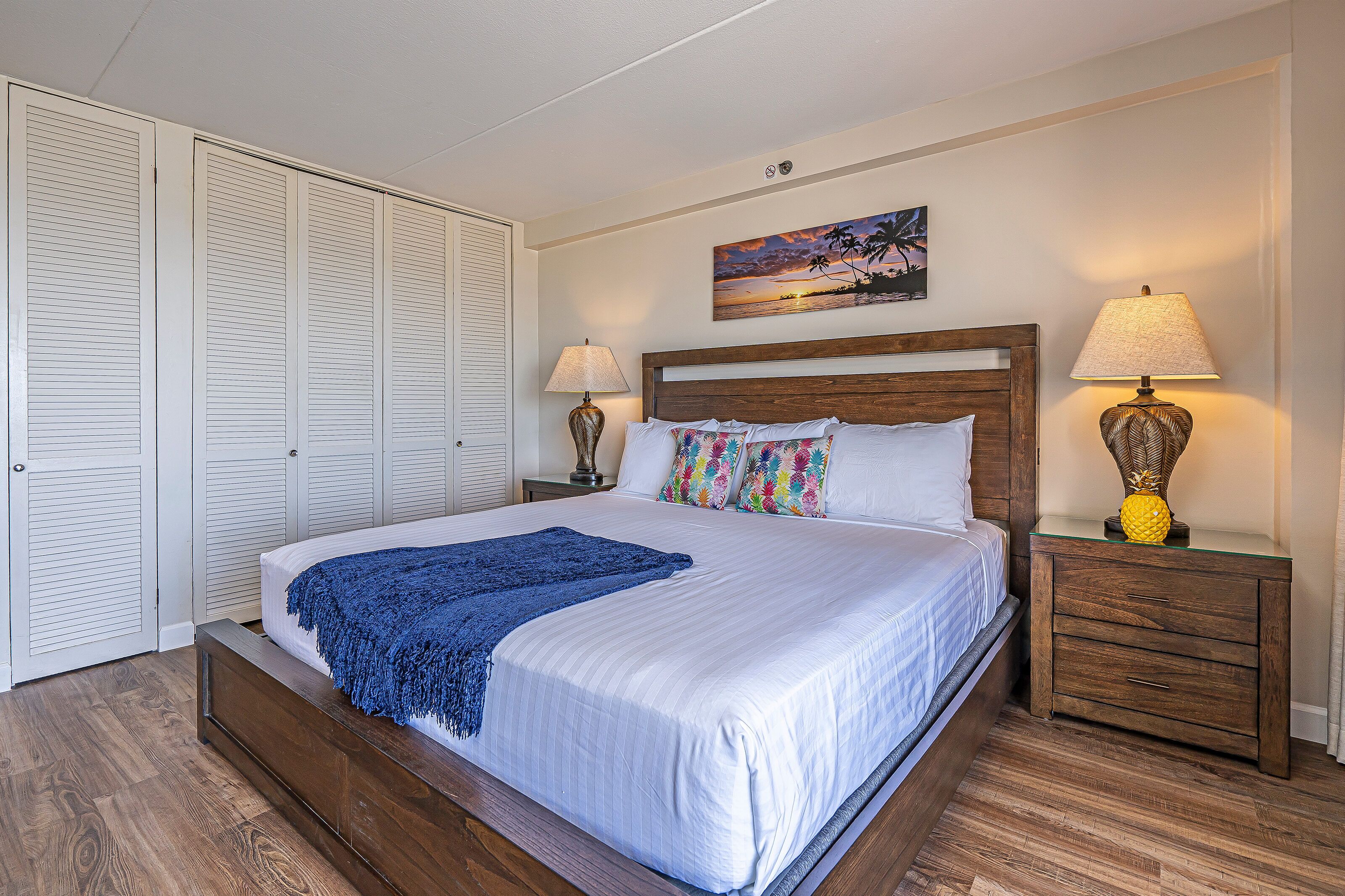 A neatly made bed with a blue throw blanket, wooden headboard, and two bedside lamps.