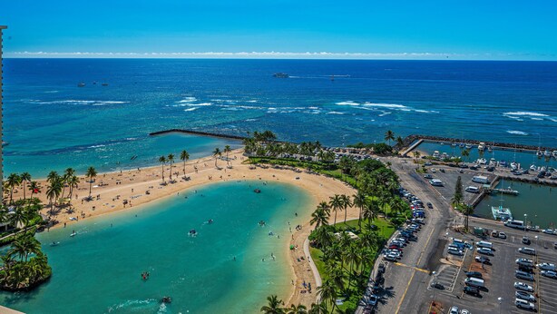 An aerial view of a beach with a parking area, boats, and a clear blue sky.