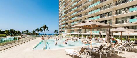 A hotel pool area with multiple levels of balconies, sun loungers, and umbrellas.