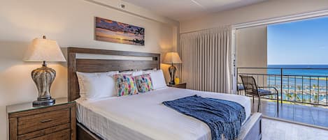 Un dormitorio con una cama grande, dos mesitas de noche, un balcón con vistas al mar y un cuadro en la pared.