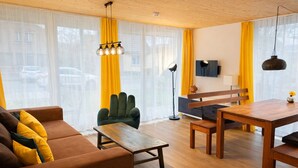 Ein modernes Wohnzimmer mit Sofa, Sessel, Esstisch und einem an der Wand befestigten Fernseher.