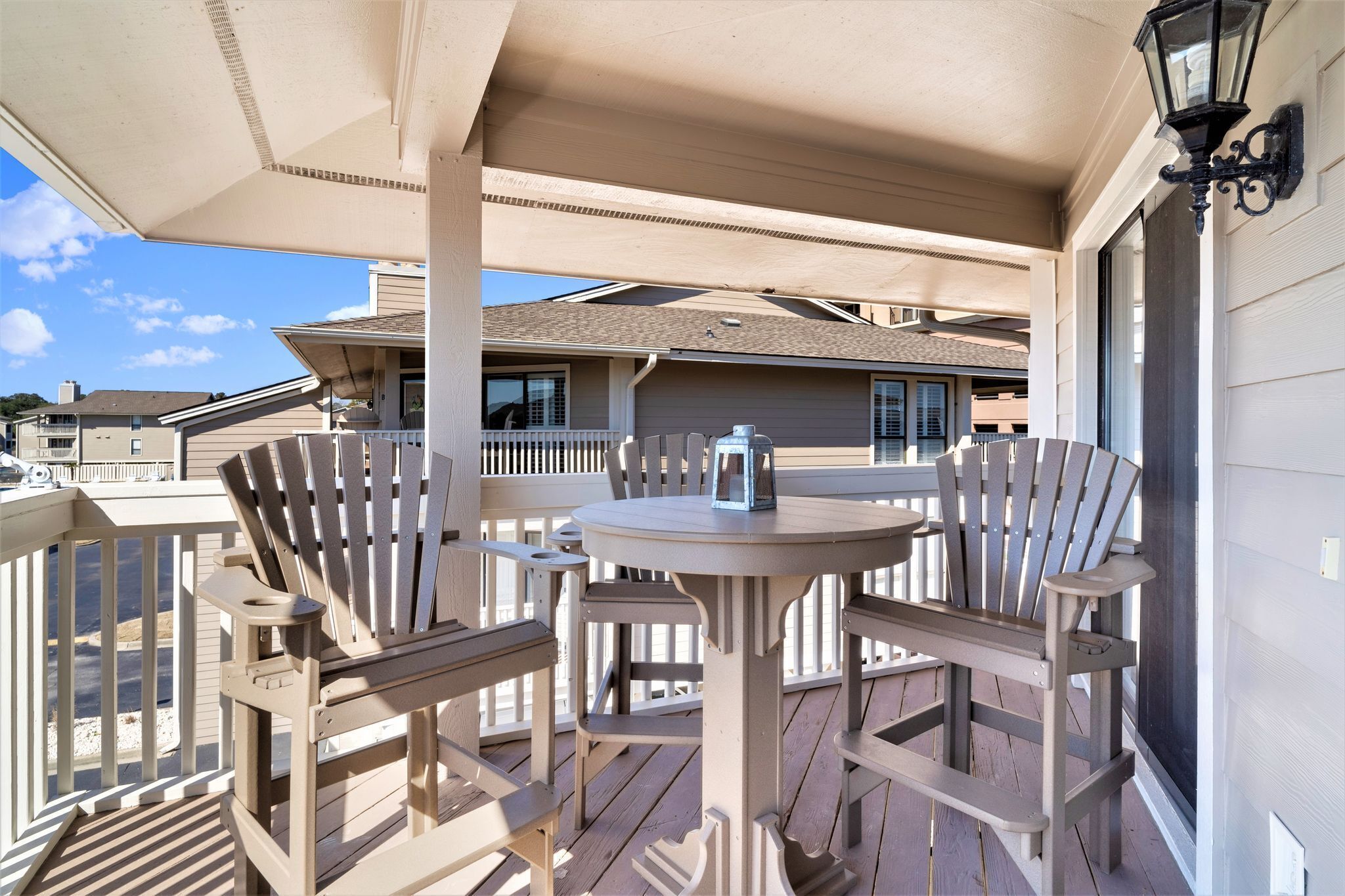 A covered outdoor seating area with a table and chairs, a lantern, and a view of neighboring houses.