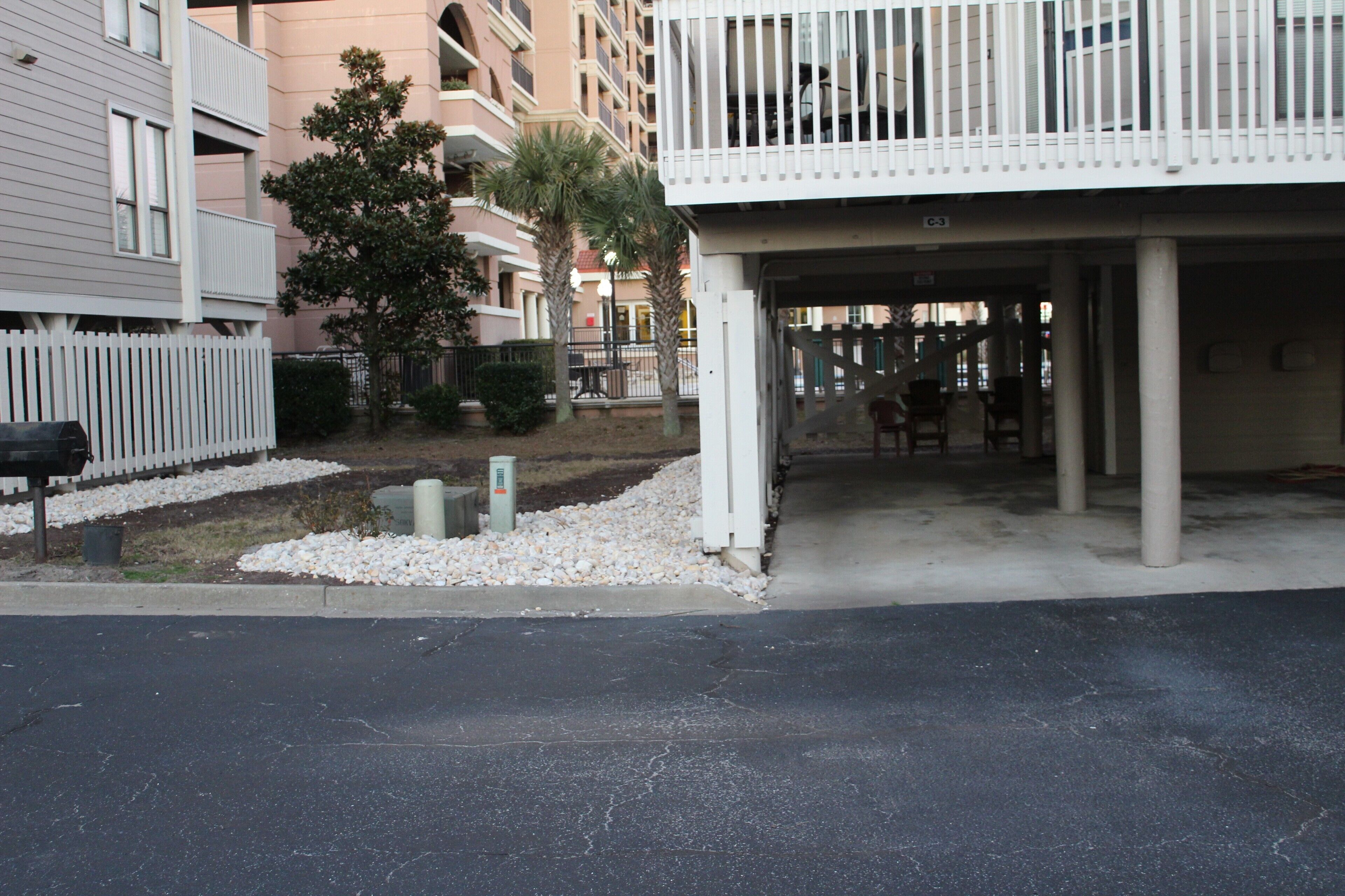A residential building with a covered parking area, a white fence, and a palm tree.