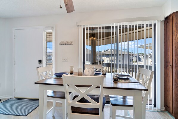 A dining area with a table set for four, white chairs, and a view through a sliding door to the outside.