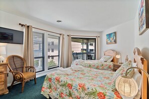 Ein Hotelzimmer mit zwei Betten, einem Sessel, einem Fernseher und einem Balkon mit Blick.