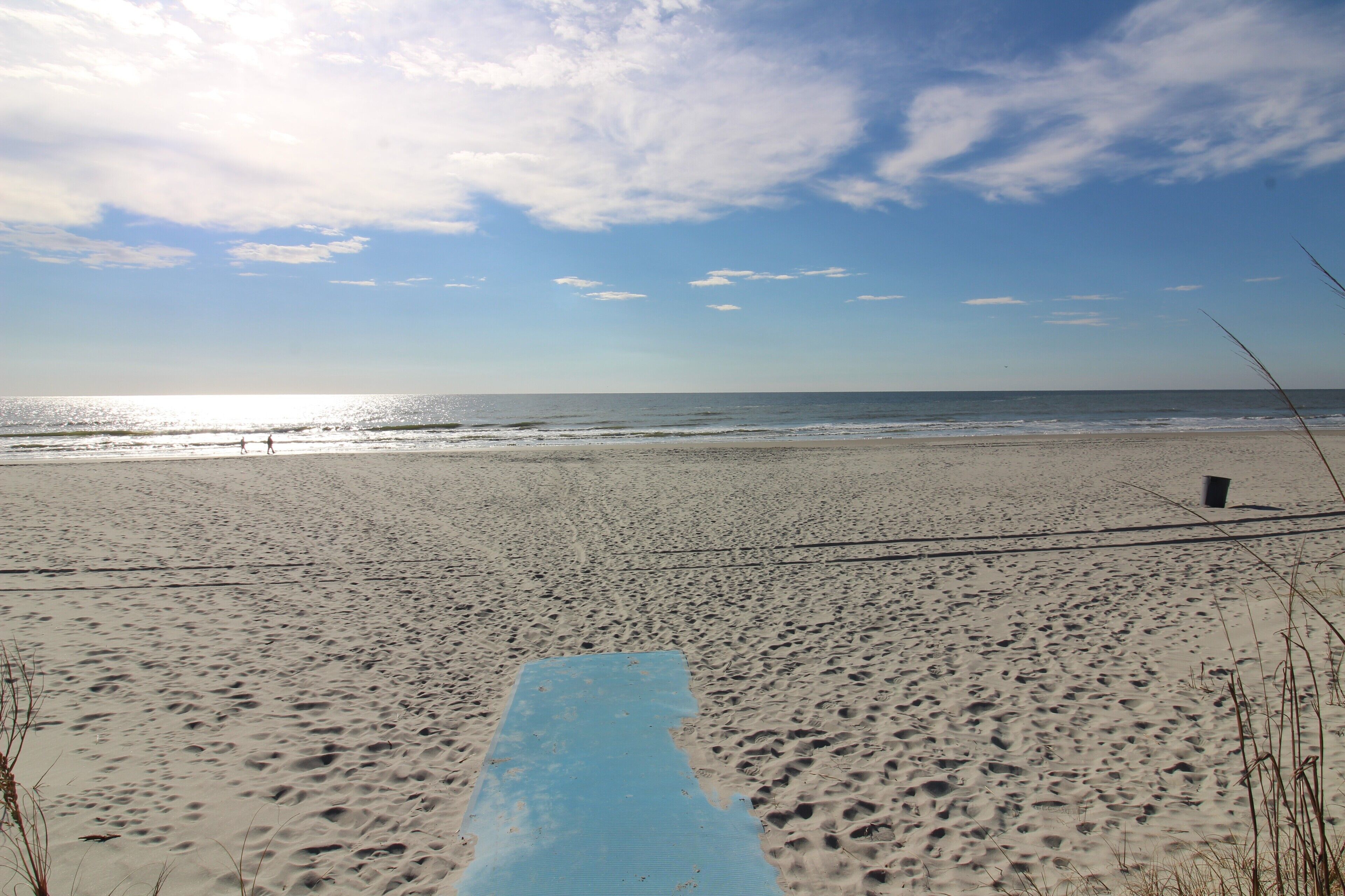 A beach with a blue mat in the foreground, sandy beach, and ocean in the background.