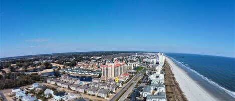 An aerial view of a coastal town with a beachfront, residential buildings, and a large hotel with multiple floors.