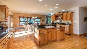 A spacious kitchen with wooden cabinets and a central island, large windows allowing natural light, and a view of the outdoors. - Fischer's Paradise (Presque Isle)