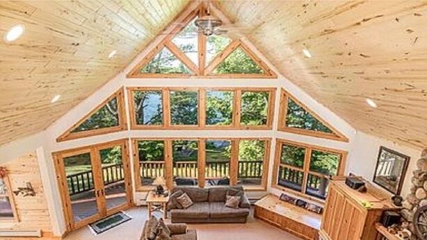 A spacious living area with a high ceiling and large windows, wooden furniture, and a fireplace. - Fischer's Paradise (Presque Isle)