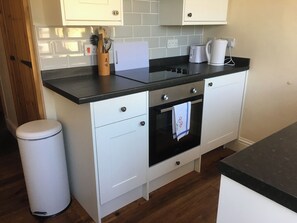 Cozinha com armários brancos, bancada preta, forno de aço inoxidável e uma lixeira.