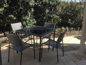 Um pátio com mesa e quatro cadeiras, cercado por vegetação e um muro de pedra.