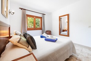 A bedroom with a bed, a window with curtains, a bedside lamp, a mirror, and a wall-mounted light switch. - 3 bedroom villa with gated pool in Pollensa, Tonia (Pollensa / Pollença)