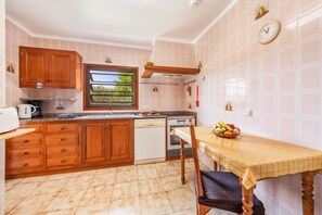 Una cocina con armarios de madera, lavavajillas, ventana y frutero sobre la mesa.