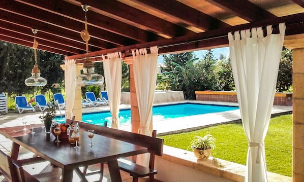 Enjoy a casual dining experience under a shaded pergola, adjacent to a swimming pool.