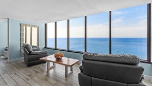 A modern living room with a large window overlooking the ocean, a leather sofa, a wooden coffee table, and a decorative mirror. - Stylish 1BR Condo w/ Bay View! Balcony, Pool, Tiki Bar, Tram to Beach & Wharf (Miramar Beach)