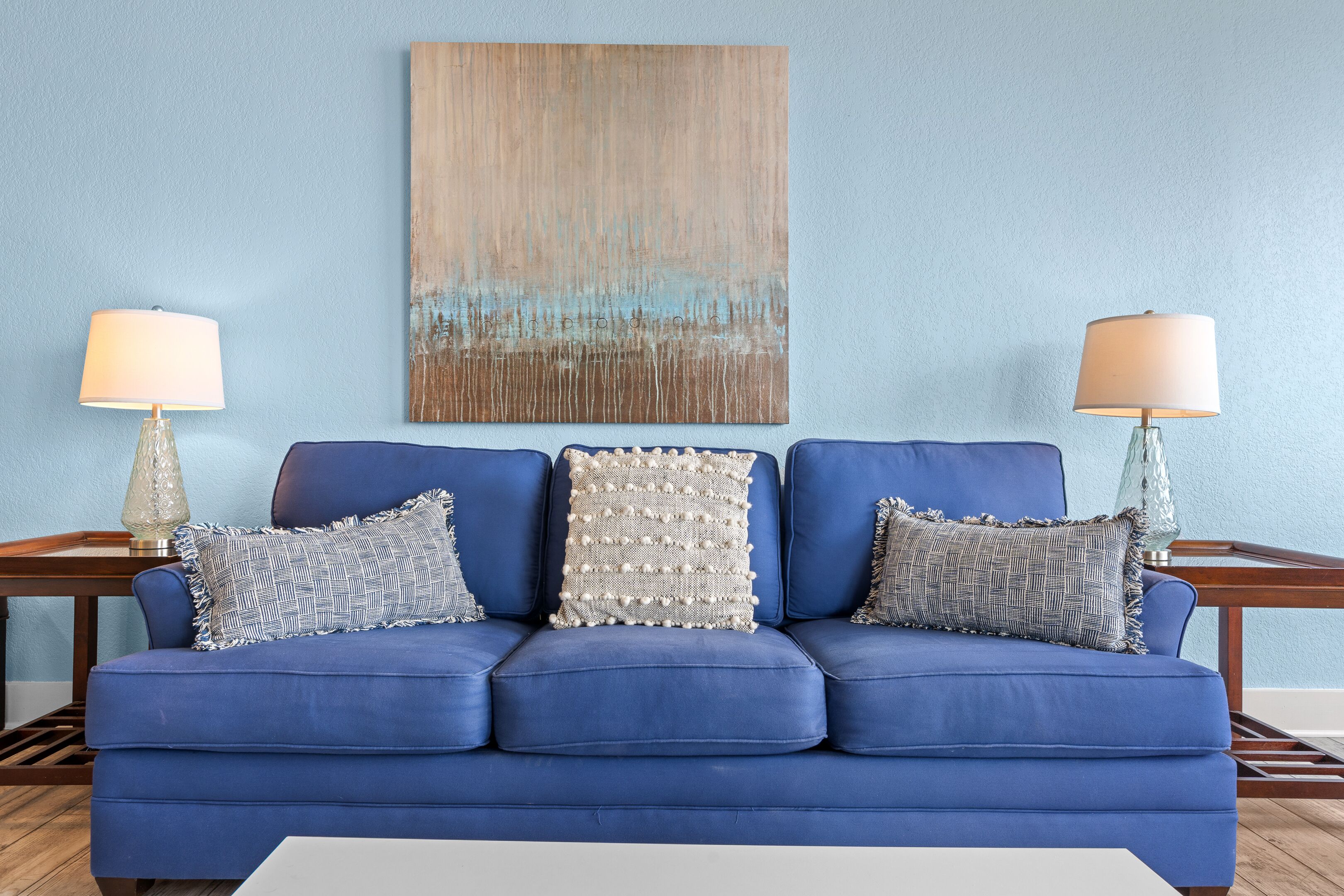 Un canapé bleu, deux lampes et un tableau accroché au mur.