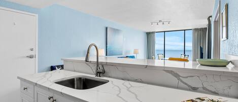 A modern kitchen with a marble countertop, a sink, and a view of the ocean through large windows.